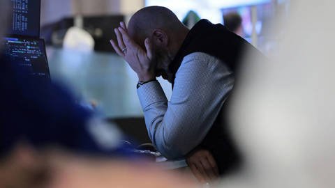 **Alt text:** Traders work on the floor of the New York Stock Exchange, monitoring market data and financial information displayed on trading screens.